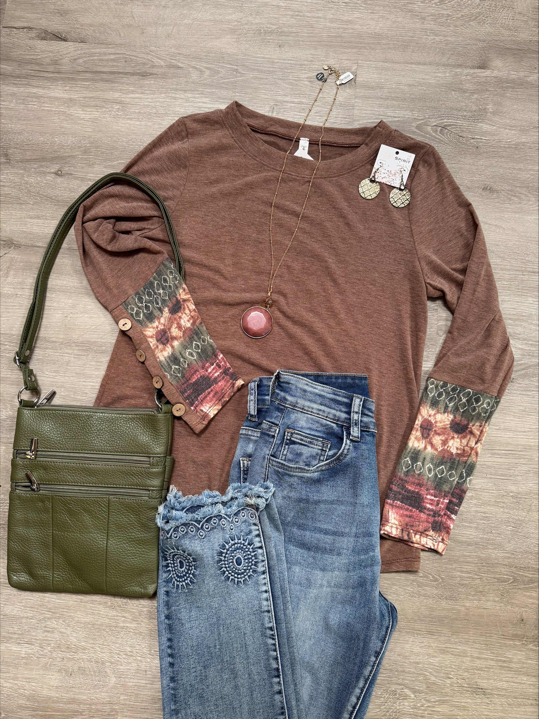 Brown long-sleeve top with patterned sleeves, green handbag, and blue jeans on a wooden surface